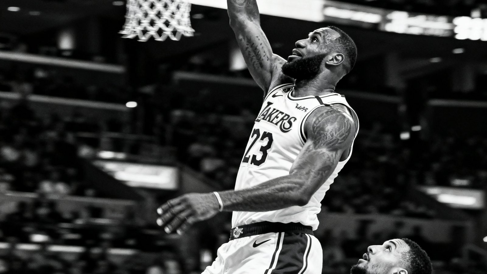 NBA赛场上勒布朗·詹姆斯在快攻中飞身扣篮，手臂伸展至篮筐上方，对手防守球员仰望的画面定格了力量与速度。